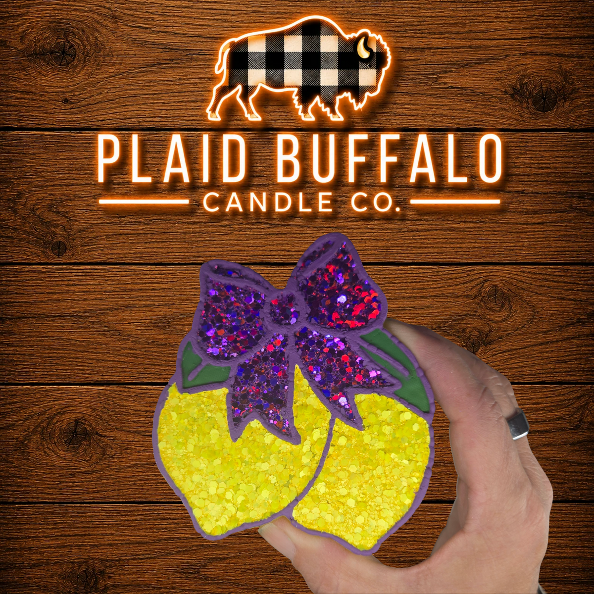 Handmade glittery lemon car freshener topped with a purple glitter bow and green leaves, displayed on a rustic wood background.