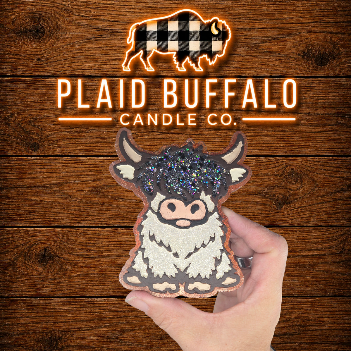 Handmade black and white Highland cow car freshener with glittery bangs, displayed on a rustic wood background.