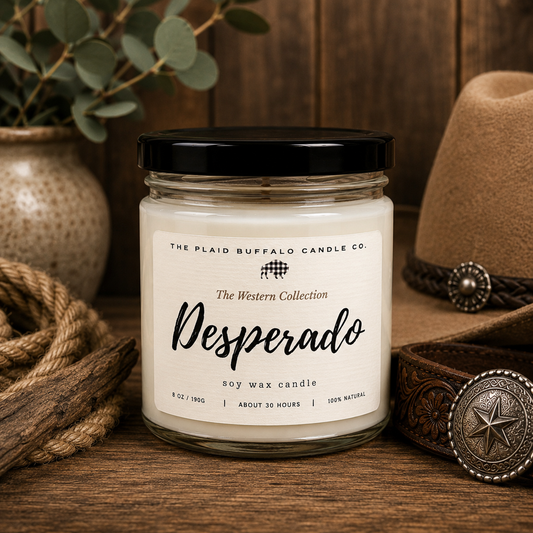 Desperado handmade soy wax candle from The Western Collection in a clear glass jar with a black lid. Displayed with a cowboy hat, leather belt, rope, and rustic wood background.