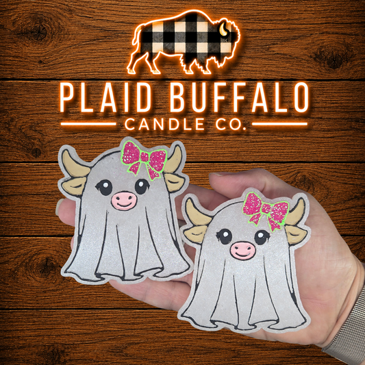 Set of two Highland cow ghost-shaped car freshies with soft white ghost bodies, cream-colored horns, pink noses, and bright pink glitter bows, displayed on a rustic wood background with the Plaid Buffalo Candle Co. logo.