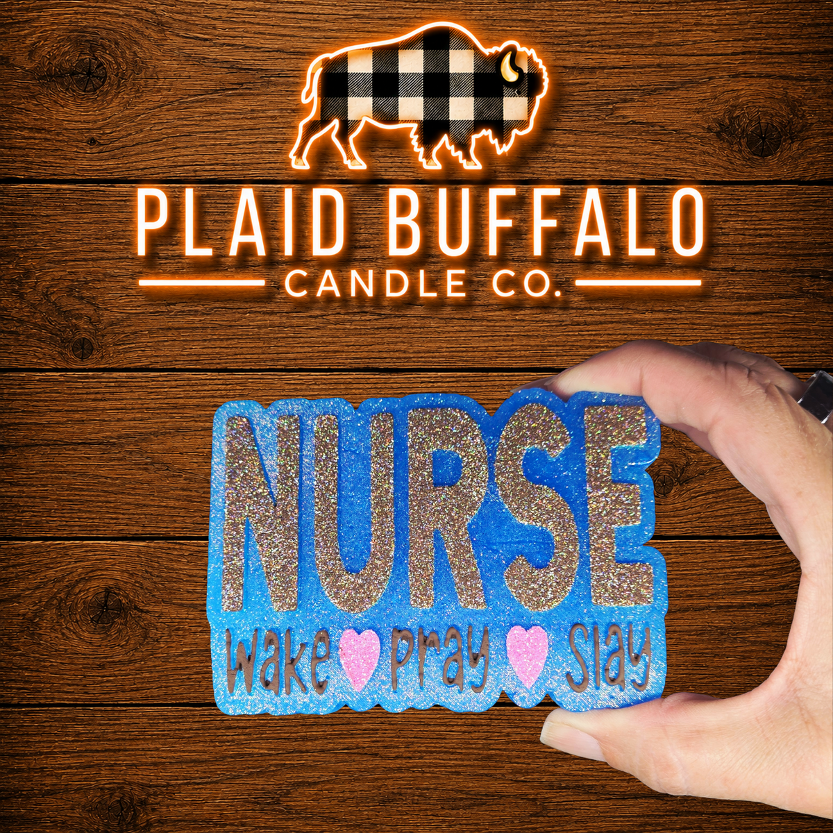 Hand holding a blue glitter nurse-themed scented car freshie featuring the words 'NURSE – Wake ♥ Pray ♥ Slay' against a rustic wood background with the Plaid Buffalo Candle Co. logo