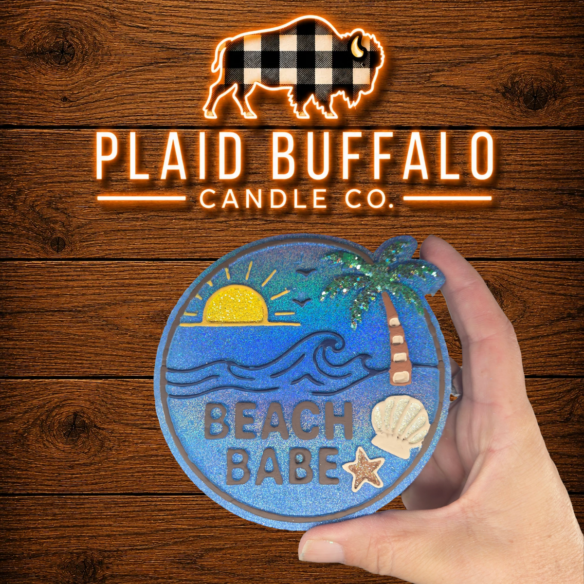 Round handmade "Beach Babe" car freshener featuring a tropical beach scene with ocean waves, sunset, palm tree, seashell, and starfish in vibrant blue tones, displayed on a rustic wood background.