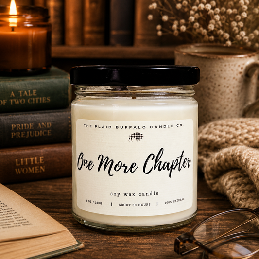 One More Chapter soy candle in a clear glass jar with a black lid, surrounded by vintage books, reading glasses, a cozy blanket, and candlelight for a relaxing reading nook.